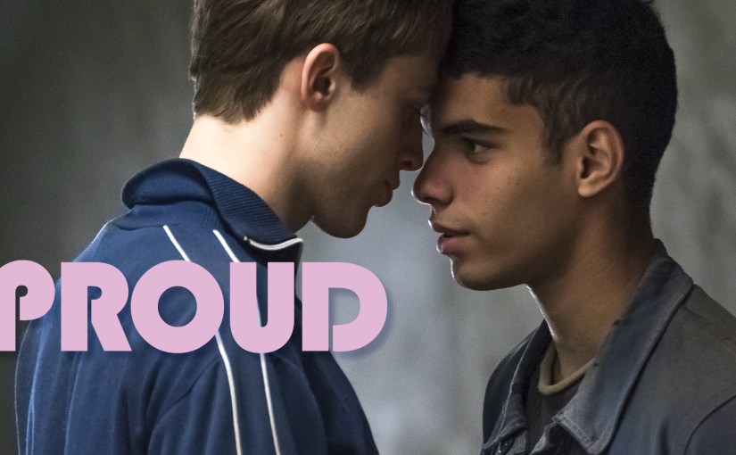 Two young men stand face-to-face in an intimate moment from the French series PROUD, with the pink PROUD title logo overlaid in the lower left.