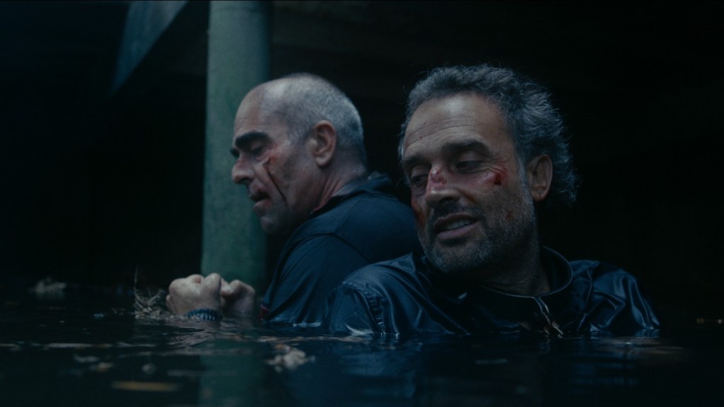 Two injured men stand chest-deep in dark water after a violent betrayal, sharing a quiet moment of vulnerability in the gay short film Concrete and Steel.