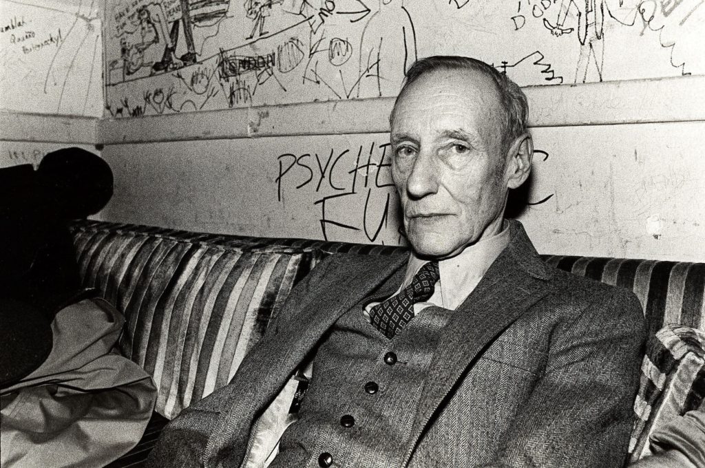 William S. Burroughs seated on a couch in front of a graffiti-covered wall