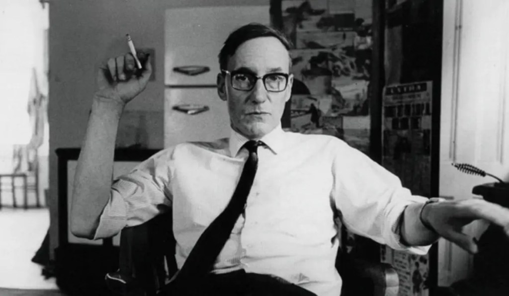 William S. Burroughs seated at his desk in a black-and-white portrait