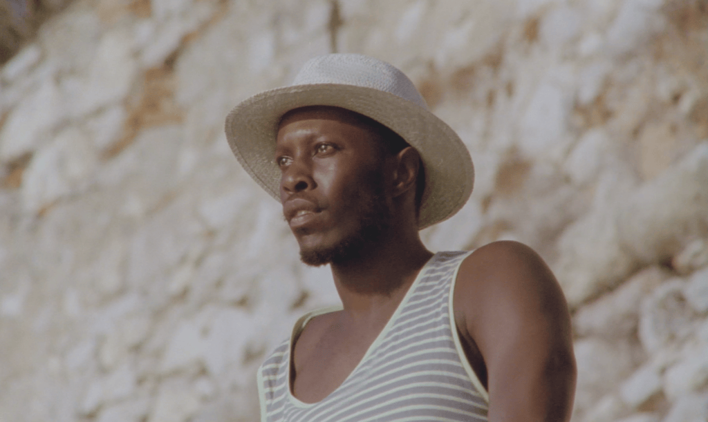 Man wearing a sun hat by the sea in A King, Gazing at the Sea