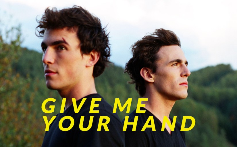 Twin brothers Antoine and Quentin stand back-to-back in the French gay film Give Me Your Hand, now streaming on Dekkoo.