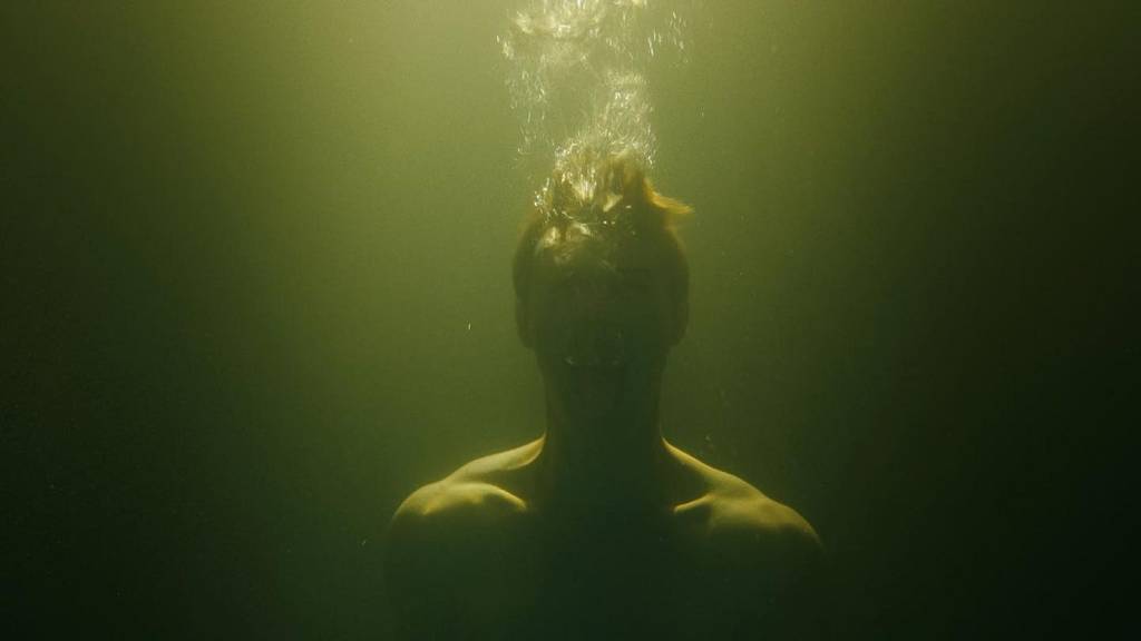 Ganymede queer horror film showing a young man submerged underwater in darkness